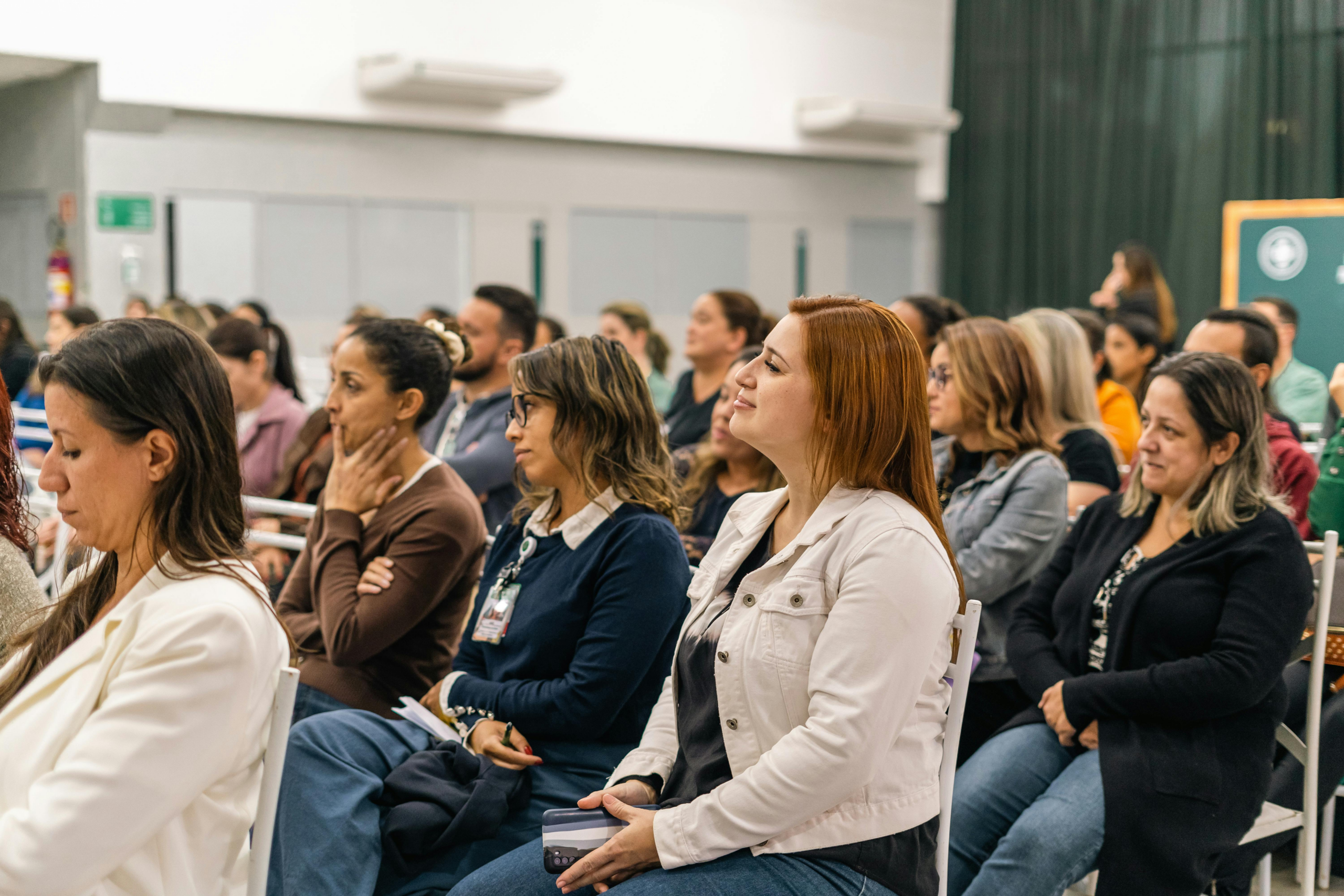 A meeting room with white walls and women of various races sitting in classroom style rows